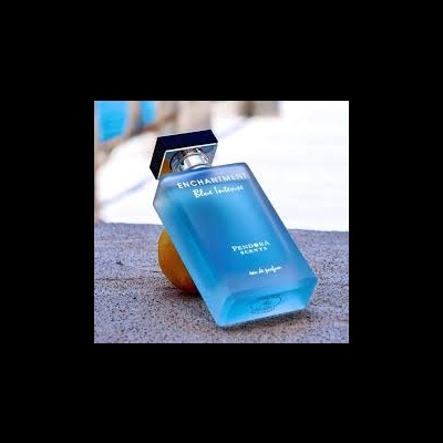 Frasco azul fosco de perfume ENCHANTMENT Blue Intense inclinado sobre uma laranja