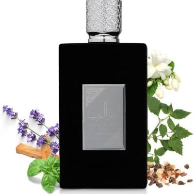 Frasco de perfume preto com tampa prateada e flores e ervas ao fundo