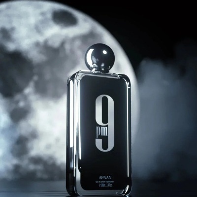 Frasco de perfume preto e prateado com o texto 9 pm e AFNAN com lua ao fundo.