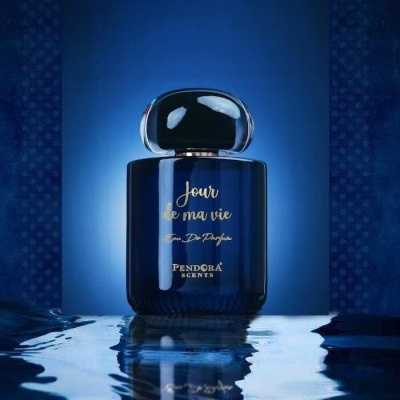 Frasco de perfume azul escuro com texto dourado sobre superfície reflexiva líquida