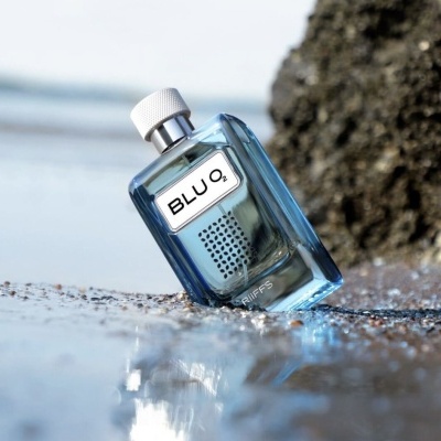 Frasco de perfume azul sobre areia molhada com rocha ao fundo
