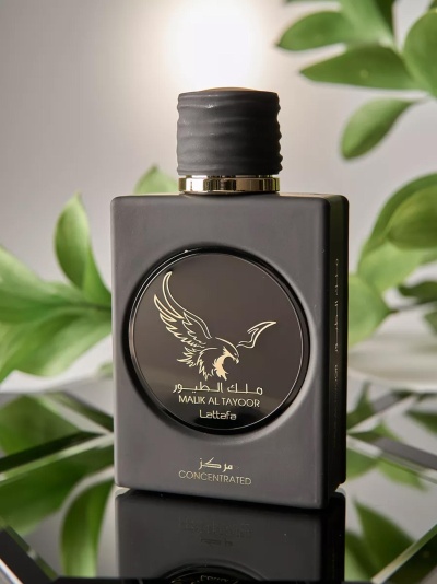 Frasco preto de perfume Malik Al Tayoor Lattafa com tampa preta e detalhes dourados, sobre superfície refletora e fundo de plantas verdes.