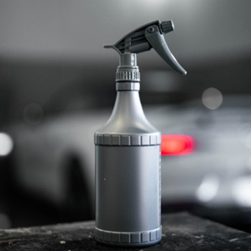 Borrifador Simples 900ml Frasco spray cinzento fosco com tampa preta sobre superfície escura com carro desfocado ao fundo