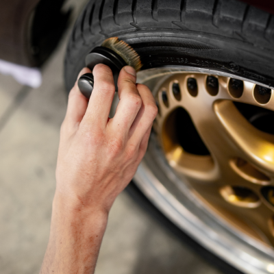 Mão a escovar pneu preto com escova de cerdas junto a roda dourada