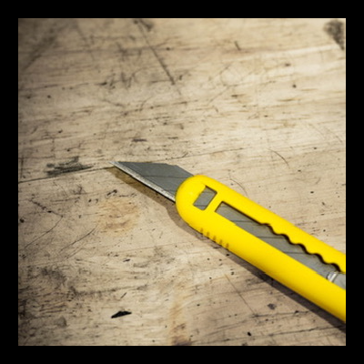 Estilete amarelo com lâmina metálica sobre madeira