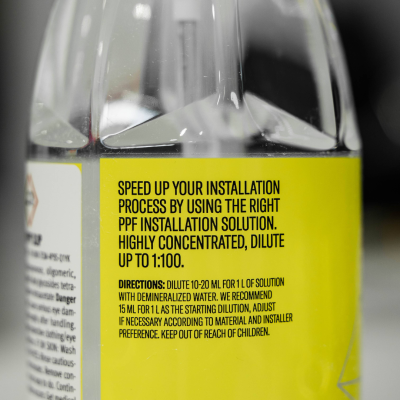 Garrafa transparente com rótulo amarelo e texto em inglês sobre uso e diluição do produto.