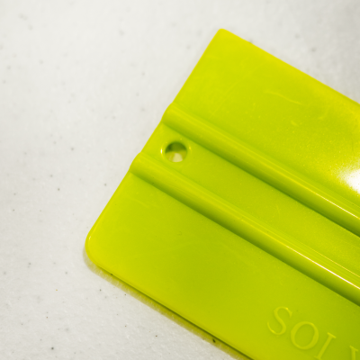 Espátula plástica verde-limão com furo redondo e texto parcial 'SOL'