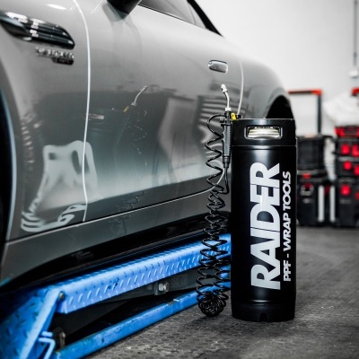 Carro cinzento num elevador azul com cilindro preto RAIDER em oficina