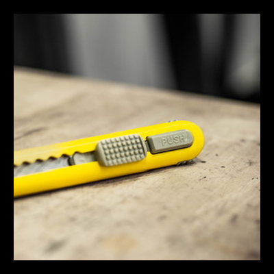 Estilete amarelo com botão cinzento PUSH em superfície de madeira