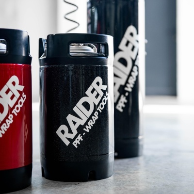 Recipientes cilíndricos plástico preto e vermelho com texto RAIDER P.F.- WRAP TOOLS em superfície clara