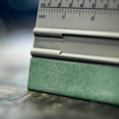 Medidor metálico com marcações em polegadas sobre uma lixa verde