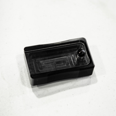 Recipiente retangular preto em plástico com pequena esfera negra no interior sobre fundo branco