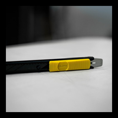 Estilete preto e amarelo com lâmina exposta sobre superfície branca