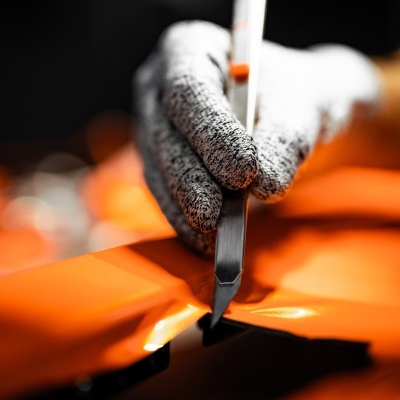 Mão com luva cinzenta a cortar material plástico laranja com ferramenta