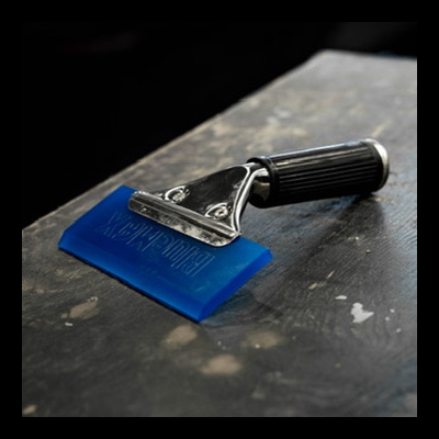 Espátula com lâmina azul e cabo preto sobre superfície escura