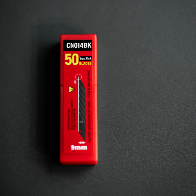 Caixa vermelha de 50 lâminas para estilete 9mm sobre superfície preta