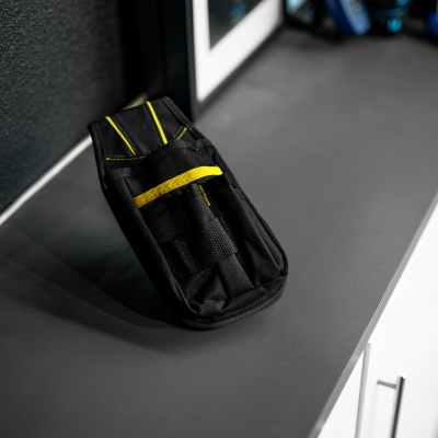 Bolsa preta para ferramentas com detalhes amarelos sobre bancada cinzenta perto de armários brancos