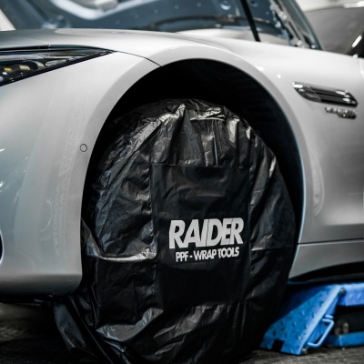 Roda de automóvel com capa preta RAIDER numa oficina com carro branco e capot aberto