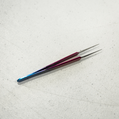 Dois ganchos metálicos com cabo em degrade azul e vermelho sobre superfície branca