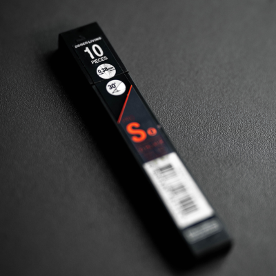 Embalagem preta comprida com texto branco e vermelho sobre superfície preta.