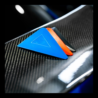 Três raspadores triangulares de plástico sobre superfície de fibra de carbono