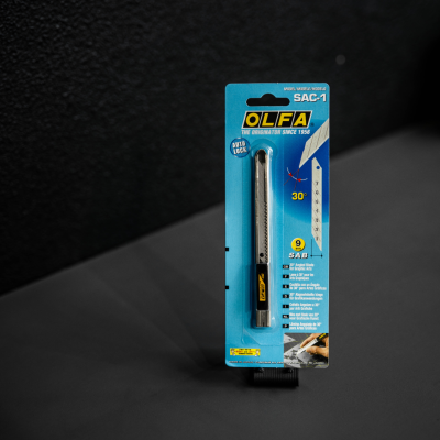 Estilete OLFA SAC-1 em embalagem azul com texto e imagem do produto