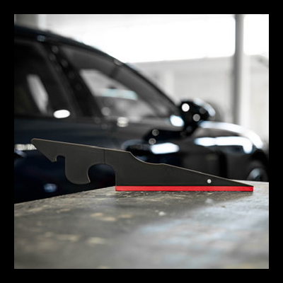 Ferramenta preta com base vermelha sobre mesa cinzenta com carro ao fundo