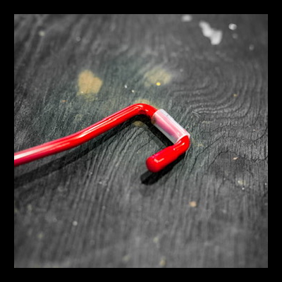 Garra metálica vermelha com gancho e tubo plástico sobre superfície escura