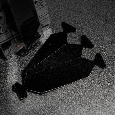 Três peças pretas geométricas sobre superfície cinza junto a embalagem com padrão geométrico