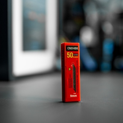Caixa vermelha de lâminas de estilete 9mm sobre superfície escura