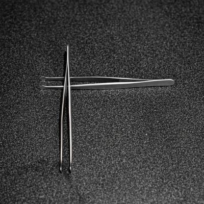 Par de pinças metálicas prateadas sobre bancada escura texturizada