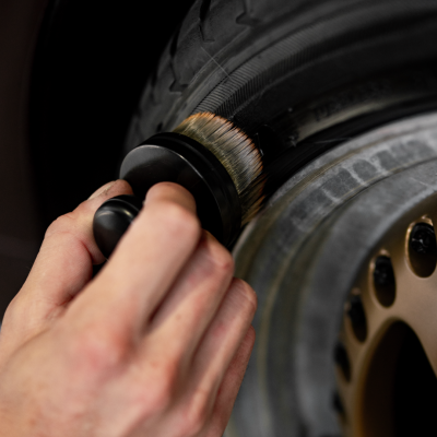 Pessoa a limpar pneu de carro com escova com cerdas marrom e brancas