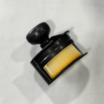 Pincel para barbear com cabo preto e cerdas amarelas sobre superfície branca