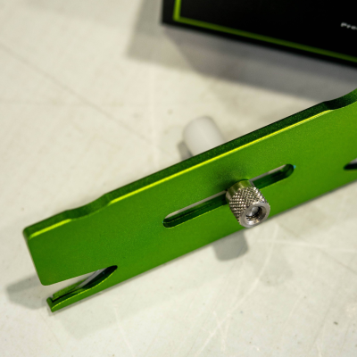 Ferramenta metálica verde com parafuso ajustável sobre superfície clara