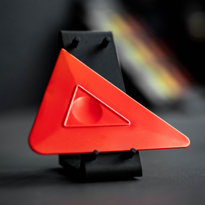 Objeto triangular vermelho em base preta sobre superfície cinzenta