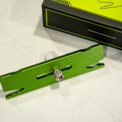 Ferramenta metálica verde com parafuso de ajuste prateado e caixa preta de fundo com detalhes verdes