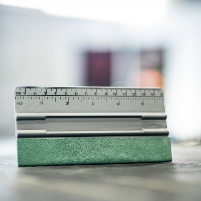 Régua metálica com base verde sobre superfície cinzenta