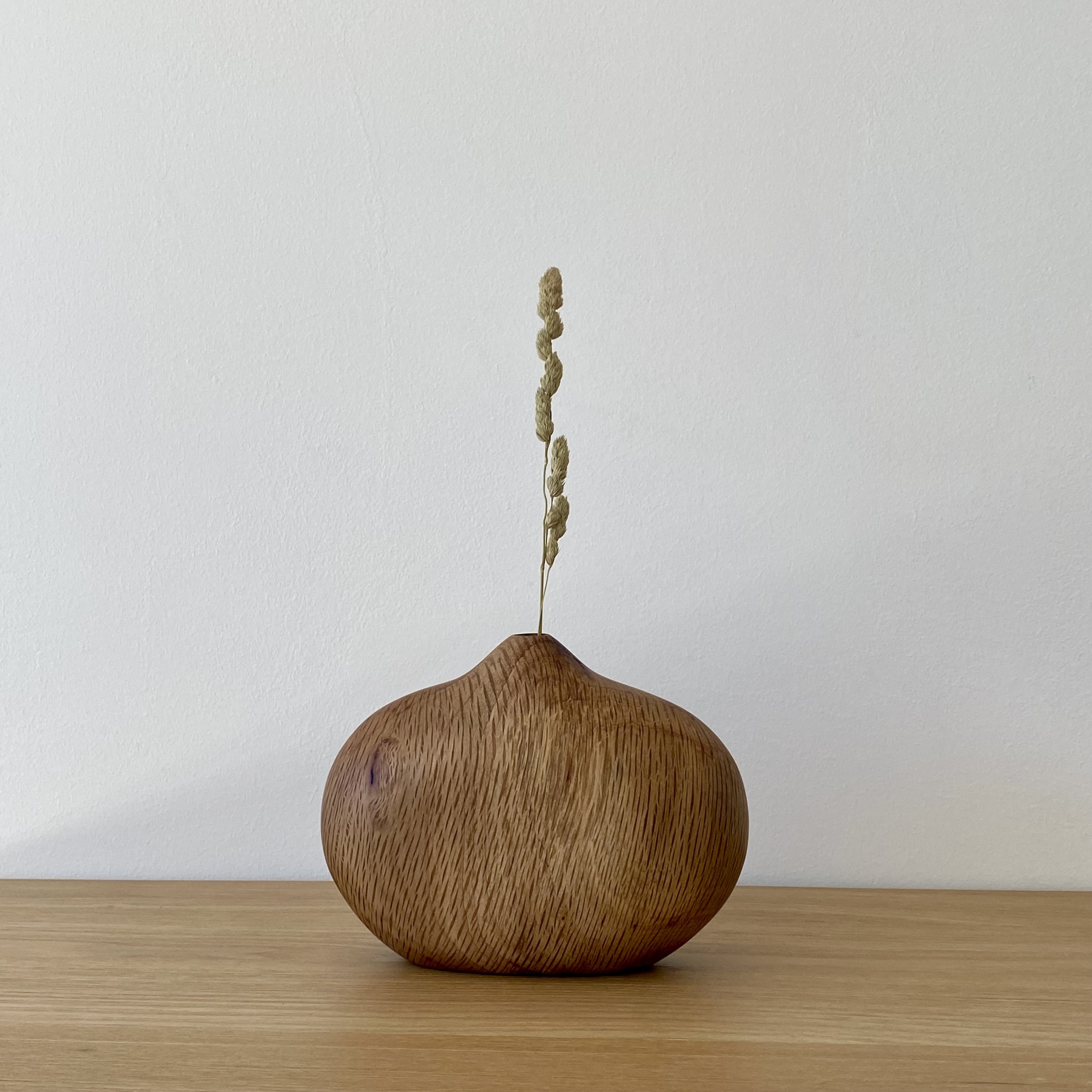 JARRA EM MADEIRA DE SOBREIRO Vaso pequeno em madeira clara com caule seco sobre mesa de madeira clara