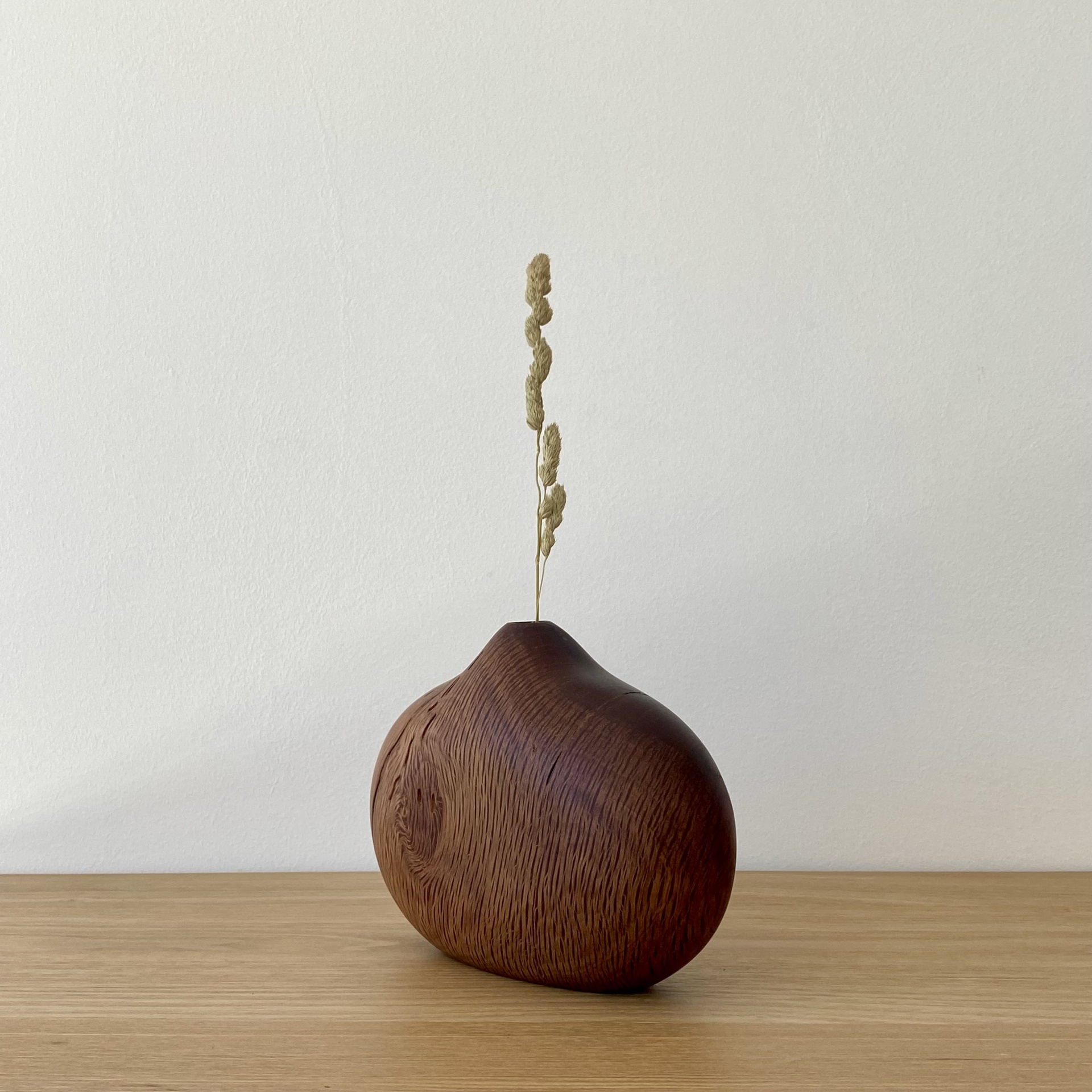 JARRA EM MADEIRA DE AZINHO Vaso decorativo de madeira castanho escuro com textura natural sobre superfície de madeira clara