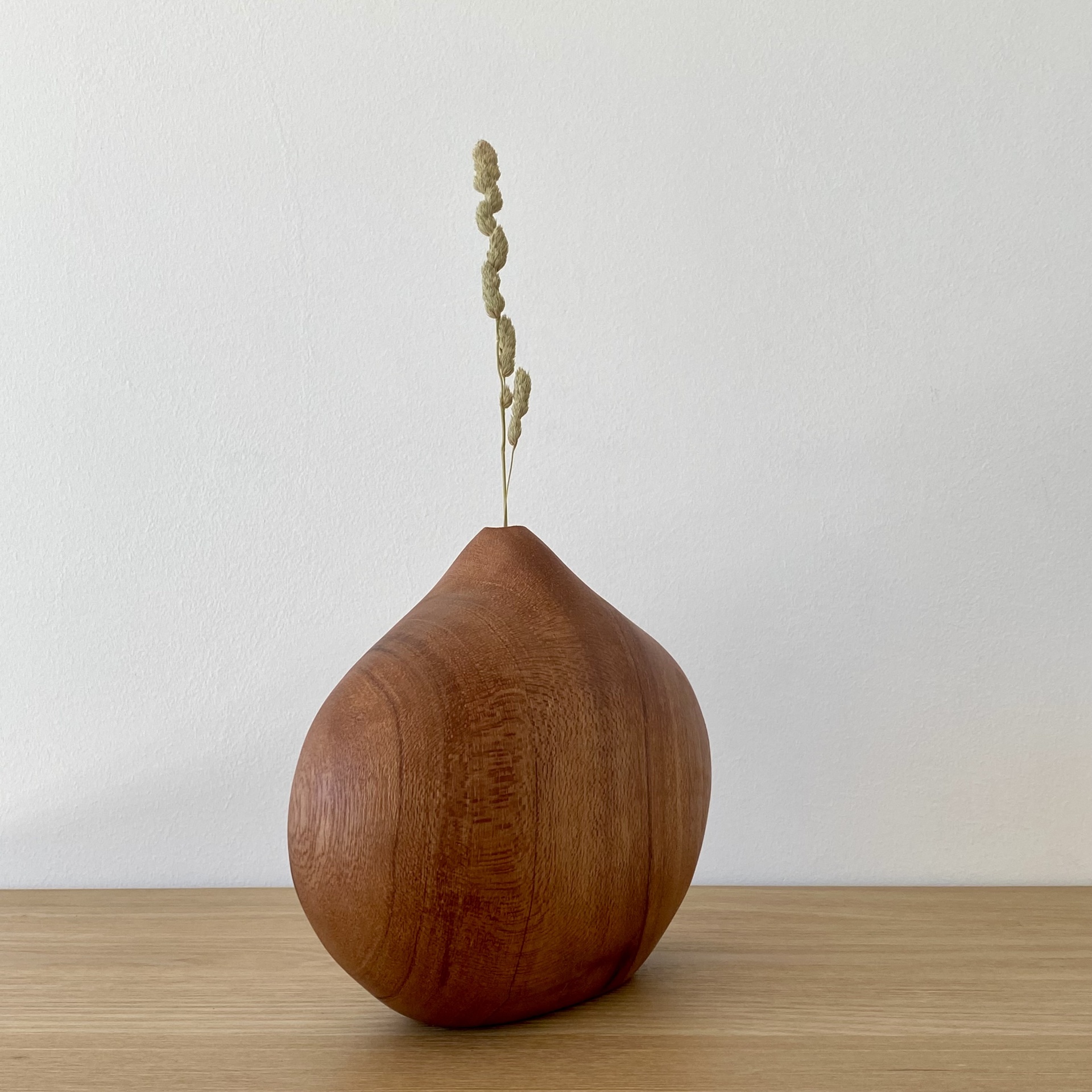 JARRA EM MADEIRA DE MOGNO Vaso decorativo em madeira castanho-avermelhada com ramo seco sobre mesa de madeira clara