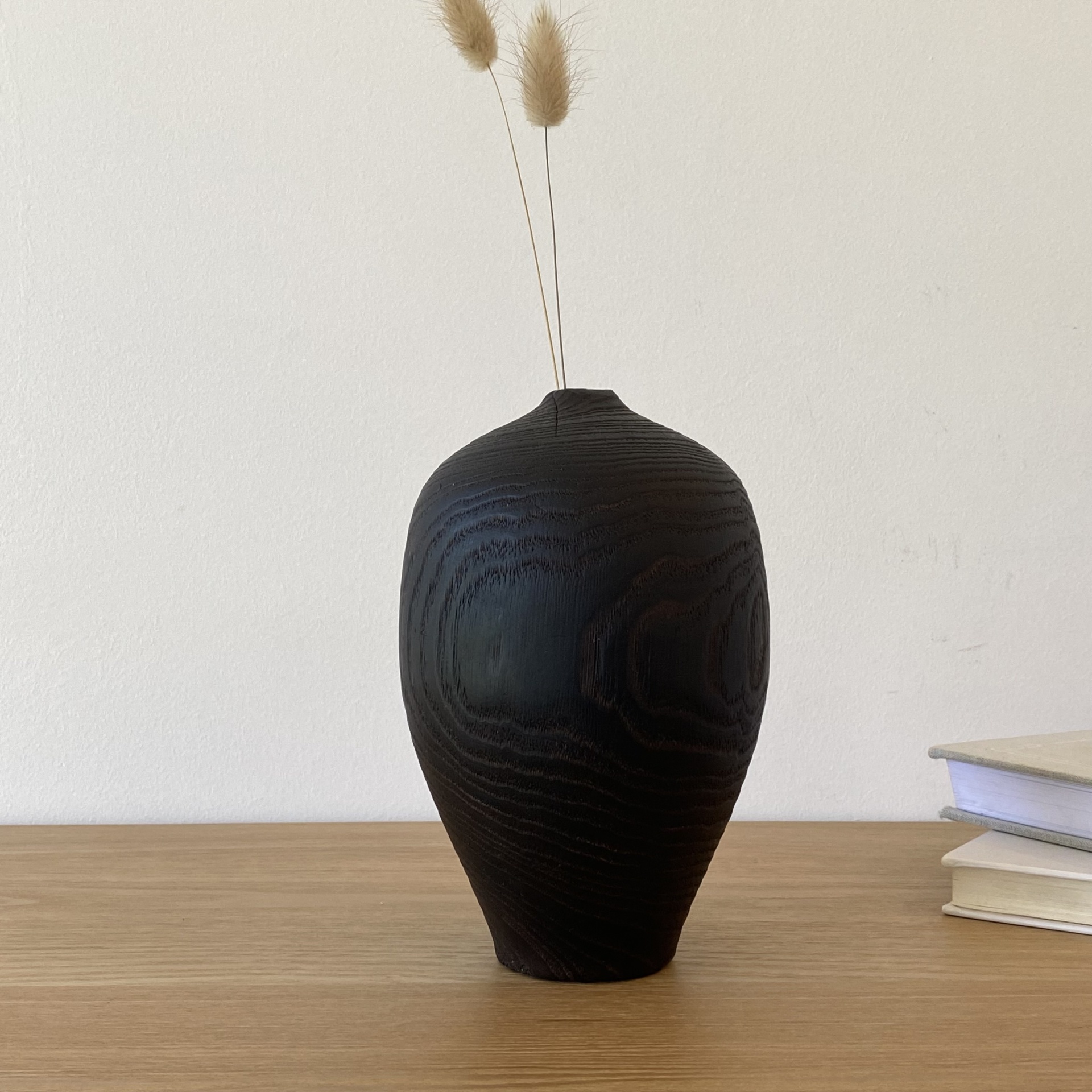 JARRA EM MADEIRA DE FREIXO QUEIMADO Vaso de madeira escura com ramos secos em cima de mesa com livros ao lado