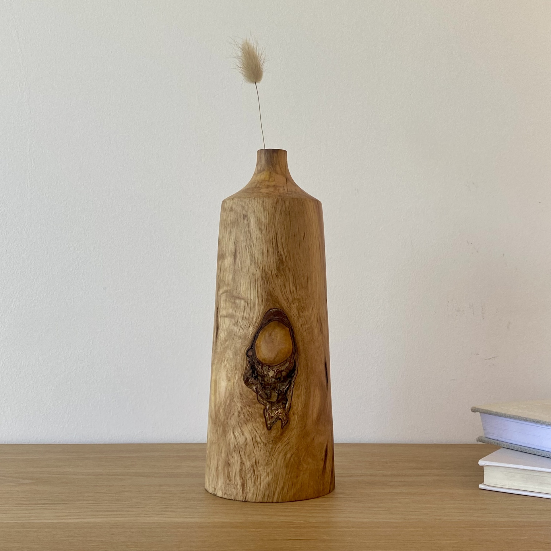 JARRA EM MADEIRA DE CIPRESTE Vaso em madeira clara com nó visível numa superfície de madeira com livros ao lado