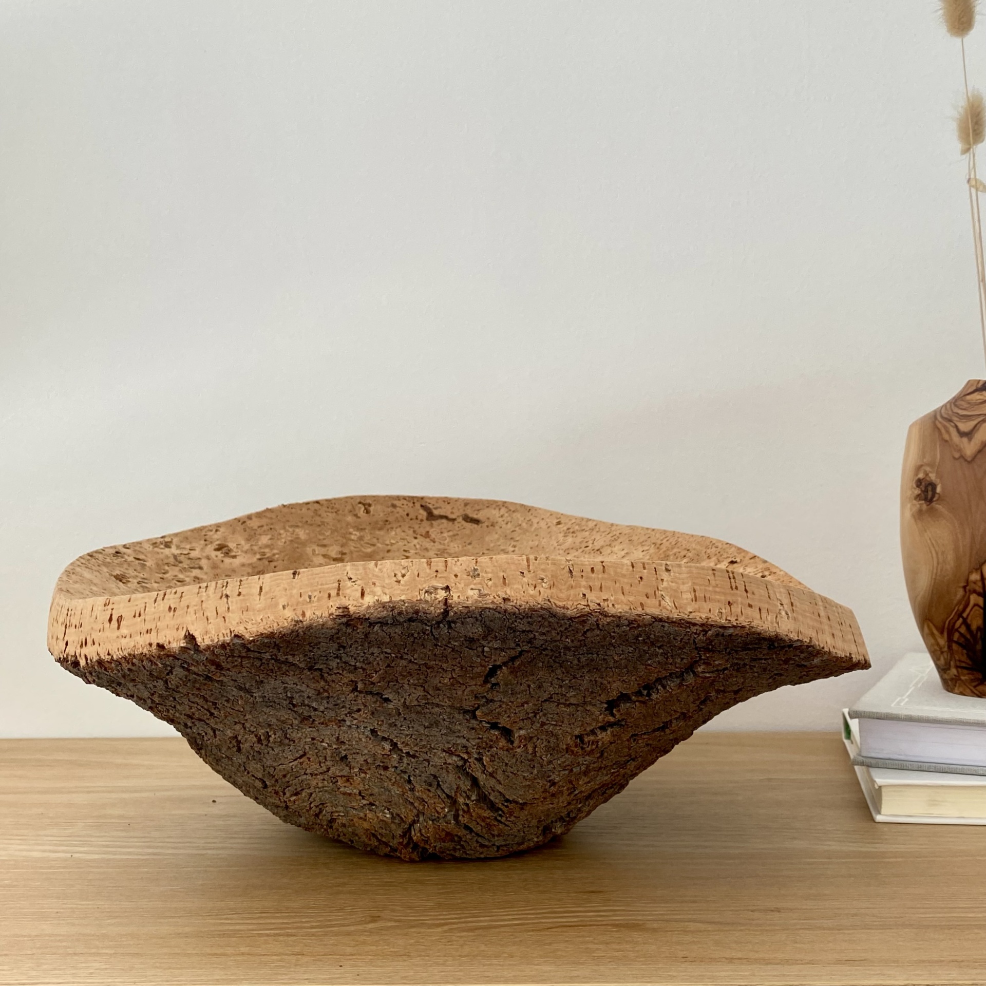 TAÇA EM CORTIÇA NATURAL Escultura decorativa de madeira natural com textura rústica sobre mesa de madeira com livros e vaso ao fundo