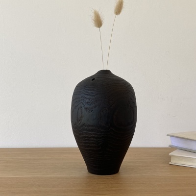 Vaso de madeira preta com textura em madeira sobre mesa de madeira junto a livros