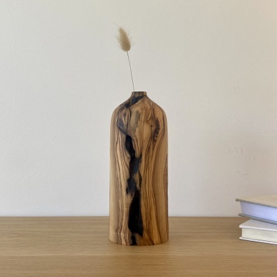 Vaso decorativo de madeira com flor seca em cima numa mesa de madeira clara