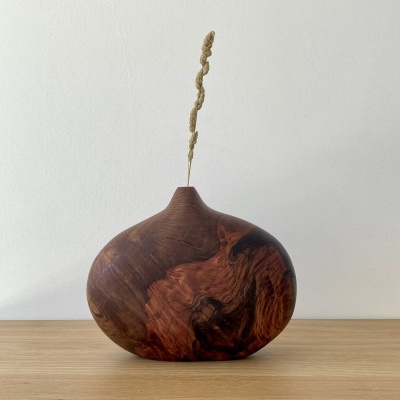 Vaso redondo em madeira com ramo seco alto numa superfície de madeira clara