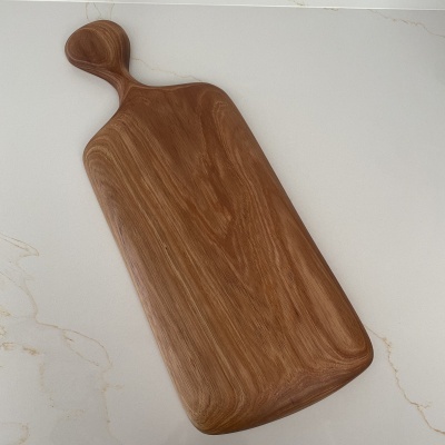 Tabua de cortar em madeira castanha com pega arredondada sobre superfície branca