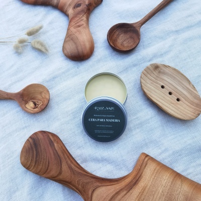 Pote de cera para madeira RAIZ-MAE com tábuas e colheres de madeira sobre tecido claro