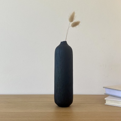 Vaso preto alto com textura e flores secas em mesa de madeira junto a livros