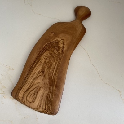 Tábua de cortar em madeira com alça sobre superfície branca com veios